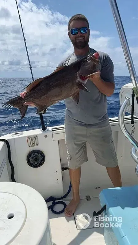 Man on a boat holding a large fish, with ocean and cloudy sky in the background.