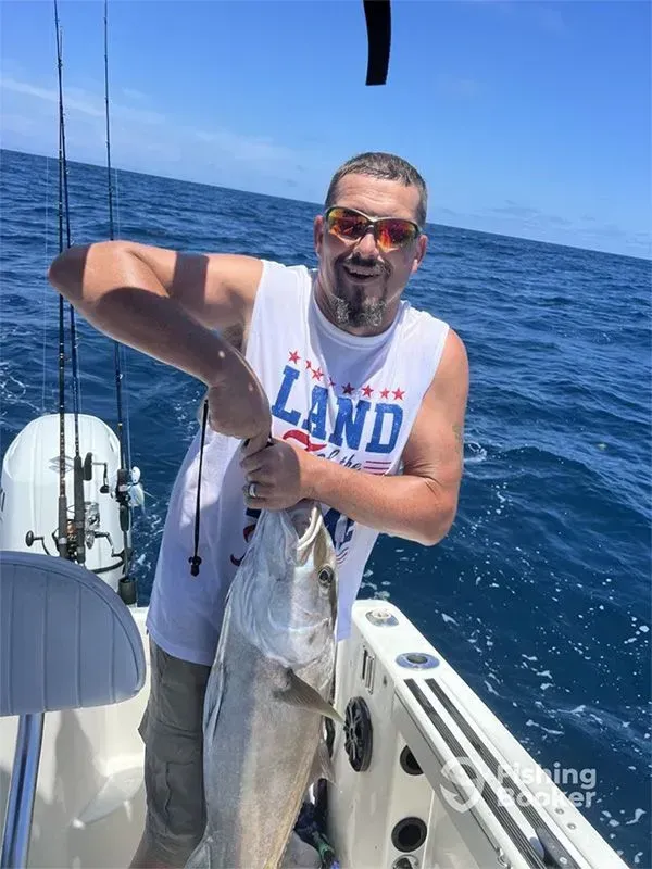 Man on a boat holding a large fish over blue ocean water under a clear sky