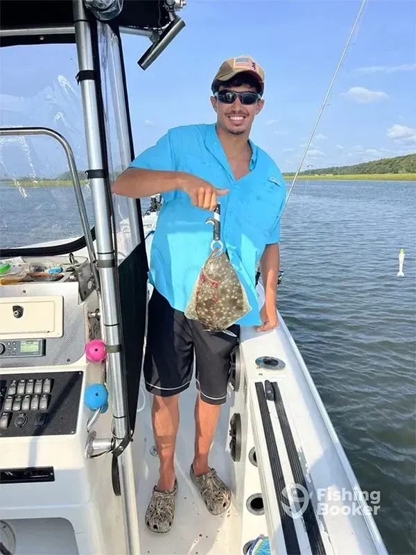 Person on a boat holding up a fish over the water, wearing a blue shirt and sunglasses.