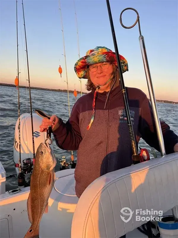 Person on a boat at sunset holding a large fish with fishing rods visible.