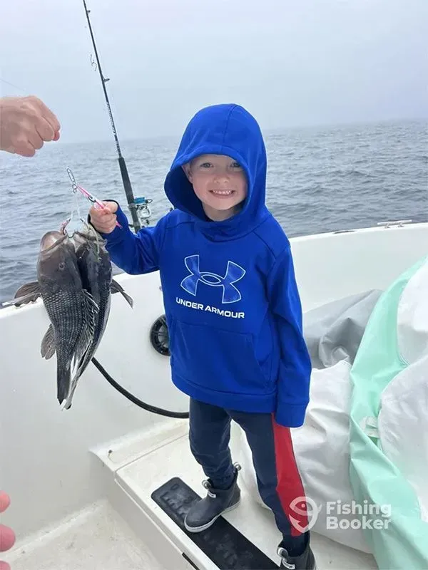 Child in a blue hoodie holding a fish on a boat at sea, smiling near a fishing rod