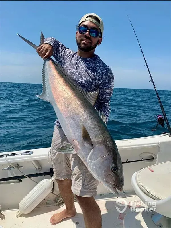 Man holding a large silver fish on a boat at sea under a clear blue sky