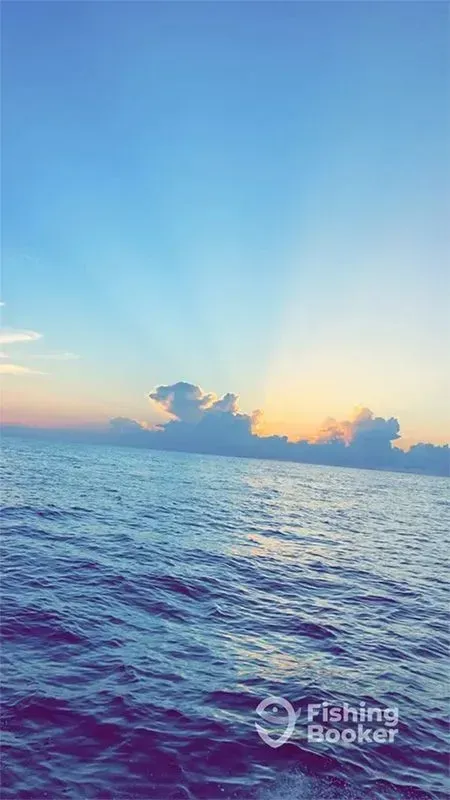 Calm ocean at sunrise with orange clouds and a blue sky over rippling water.