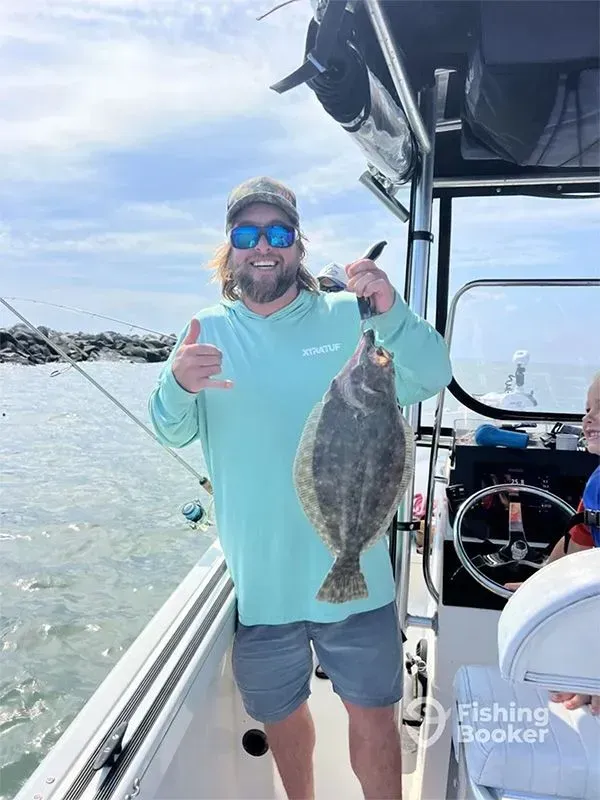 Man on a boat smiles and gives thumbs up while holding a large fish over the water.