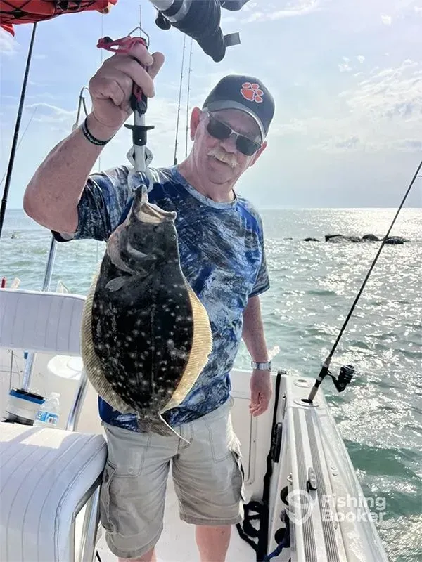Person holding up a large fish on a boat at sea, wearing a cap and sunglasses.