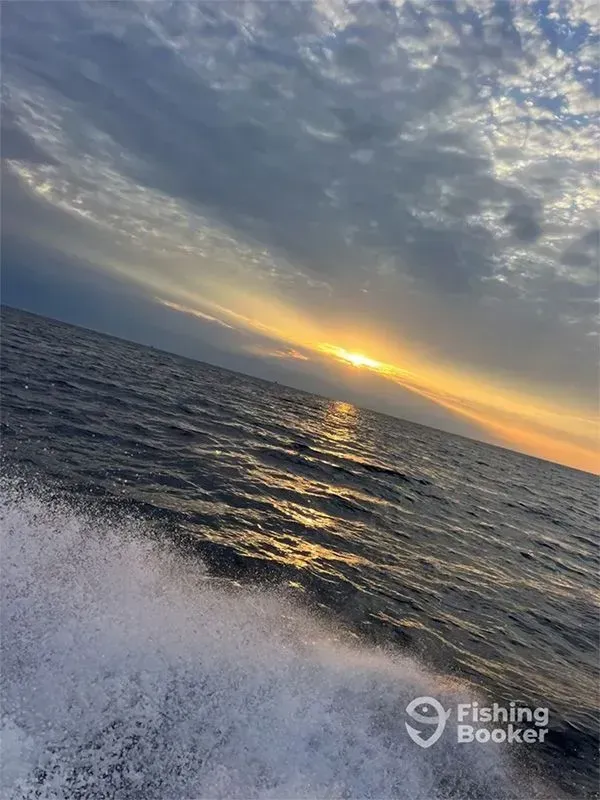 Sunset over choppy ocean waves, with a fishing boat wake in the foreground.