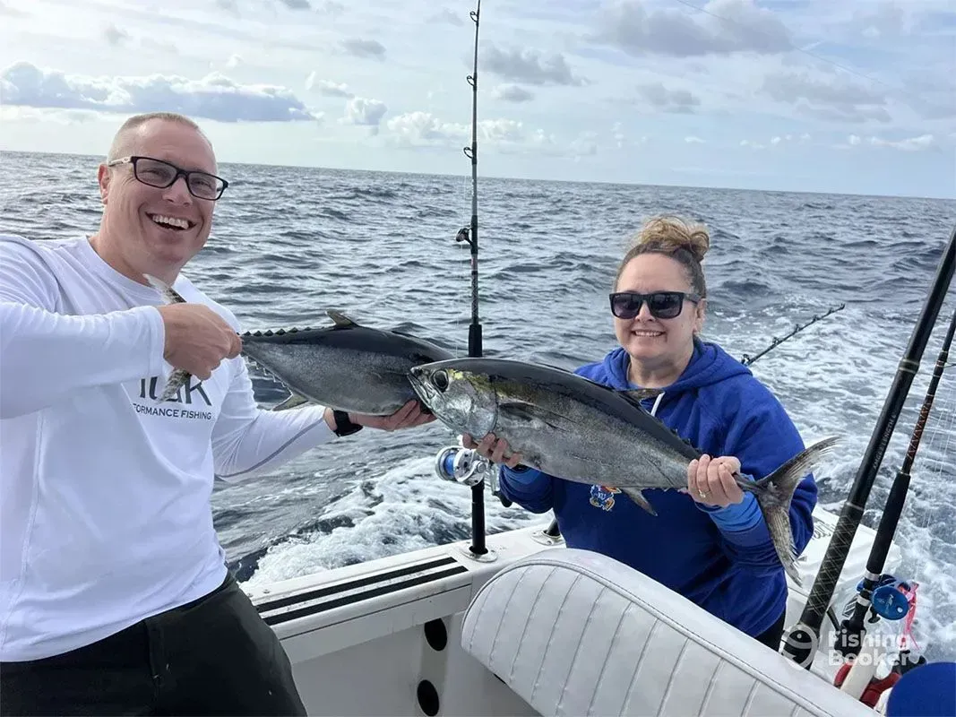 Two people on a boat holding a large fish with fishing rods and the ocean behind them