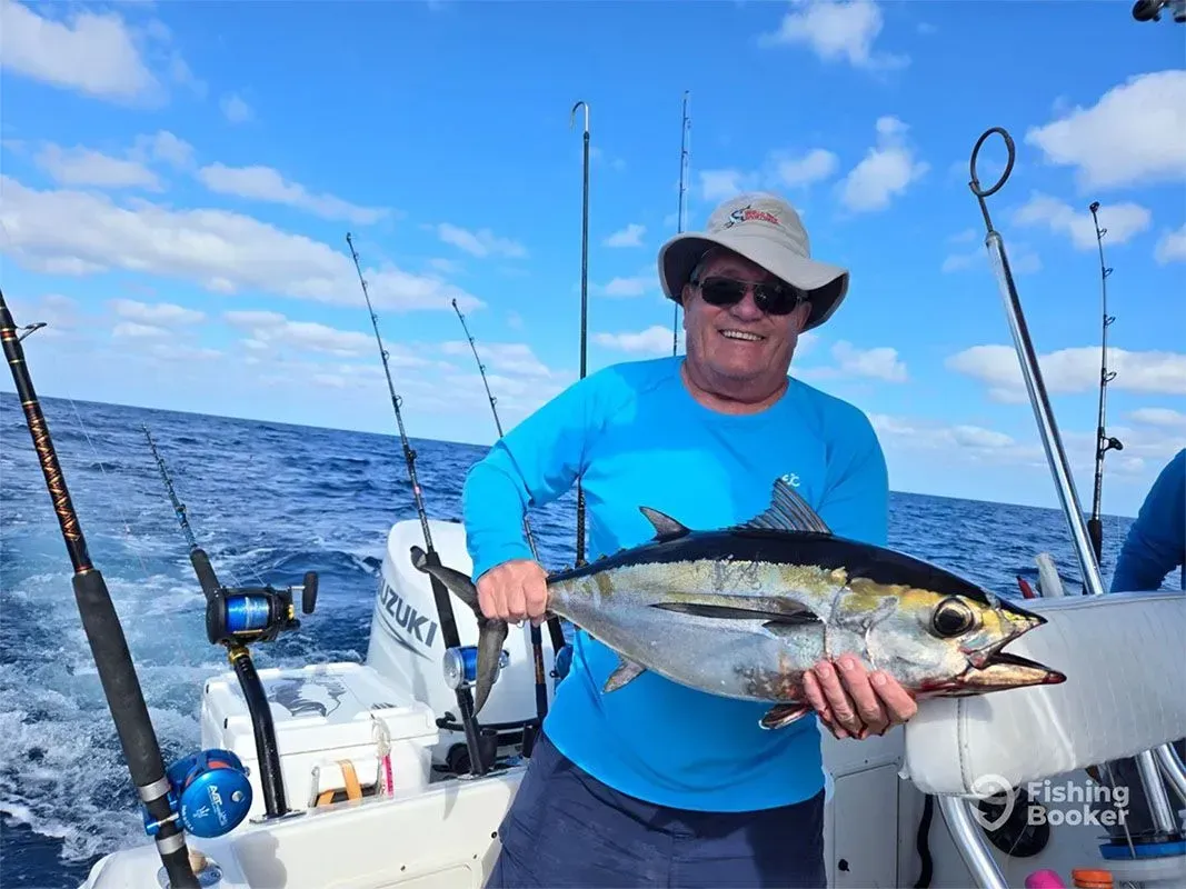 Angler on a boat holds a large tuna against a blue ocean sky.