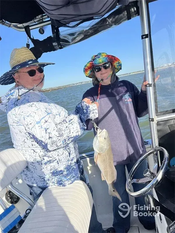 Two people on a boat hold up a fish on a sunny day on the water.