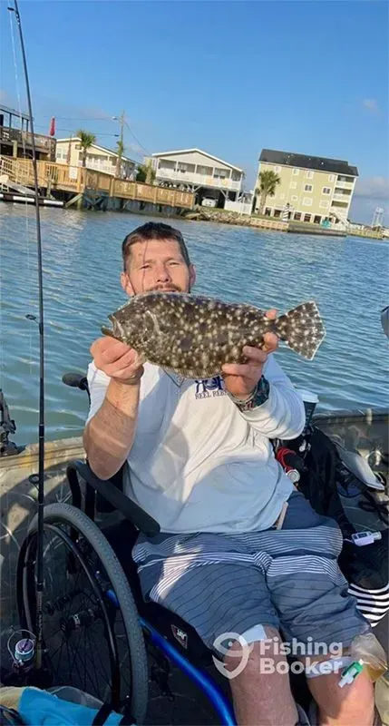 Person in a wheelchair holds up a large fish near the water at a marina.