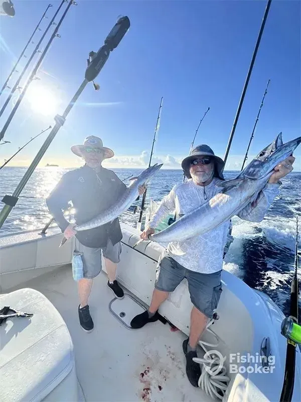 Two anglers on a boat holding large silver fish under a bright blue sky