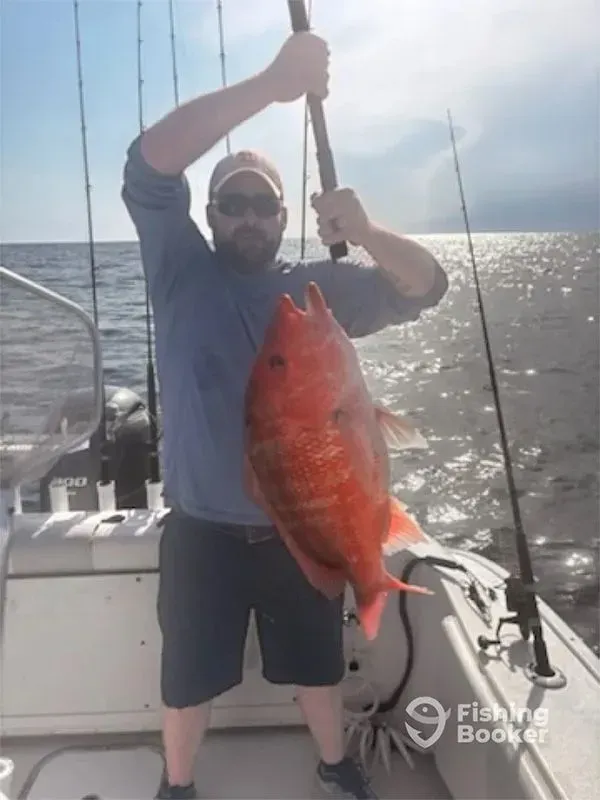 Person on a boat holds up a large red fish over the ocean.