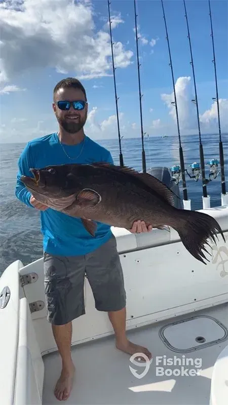Man holding a large fish on a boat at sea, wearing a blue shirt and sunglasses.