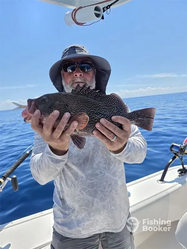 Angler on a boat holding a large black fish with the ocean in the background