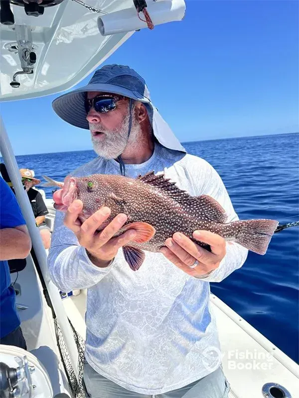 Man holding a large fish on a boat in bright blue ocean under a clear sky
