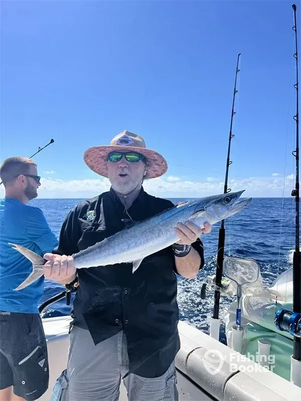 Two anglers on a boat, one holding a large silver fish on a sunny ocean trip.