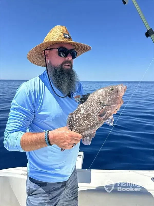 Angler in blue shirt and straw hat holding a fish on a boat at sea under a clear sky