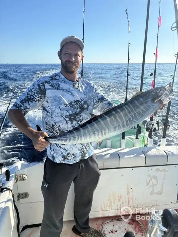 Man on a boat holding a large striped fish, with ocean and fishing rods in the background.
