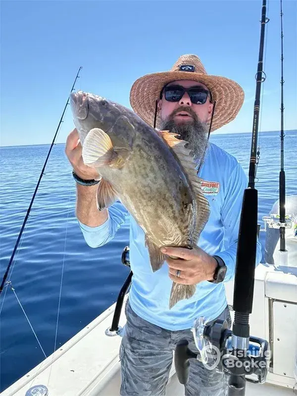 Angler on a boat holding a large fish on open water under a clear blue sky