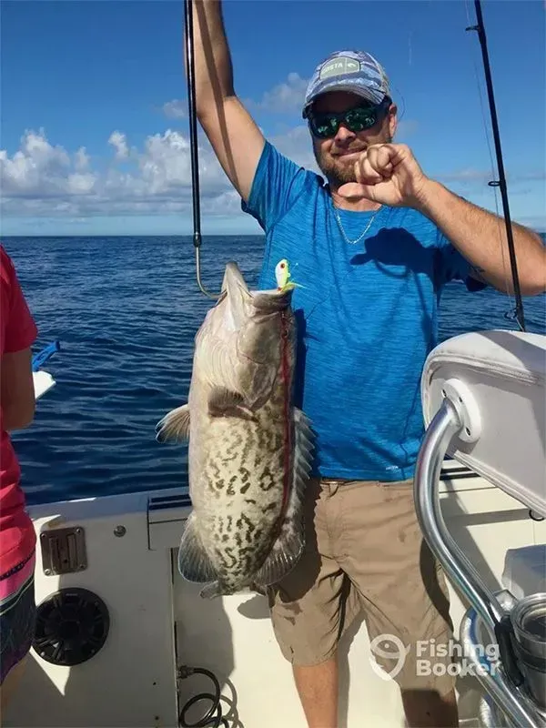 Man on a boat holding up a large fish against a blue ocean and sky