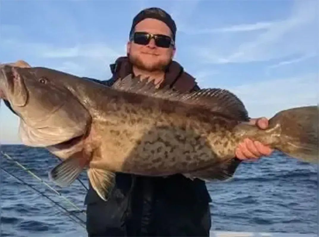 Man holding a large spotted fish on a boat with the ocean behind him