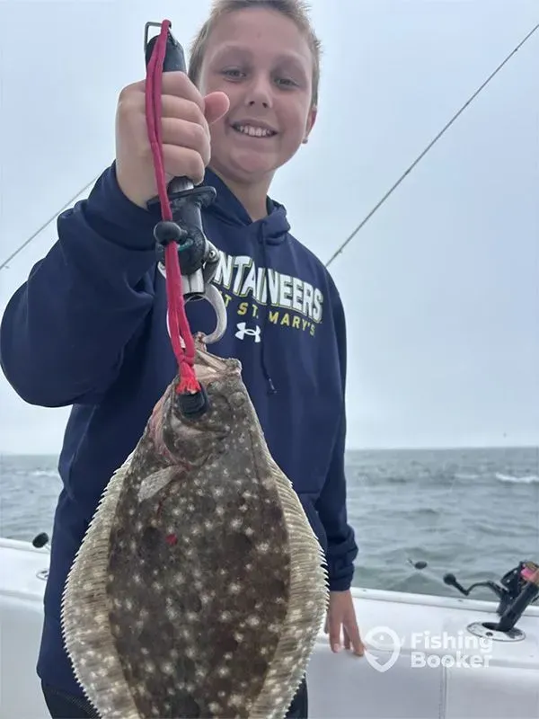 Smiling child holds a fish by a red string on a boat at sea, with overcast sky.