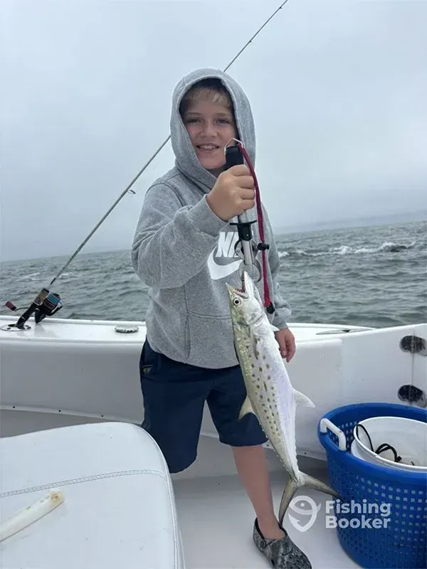 Smiling child in gray hoodie holding a fish on a boat at sea