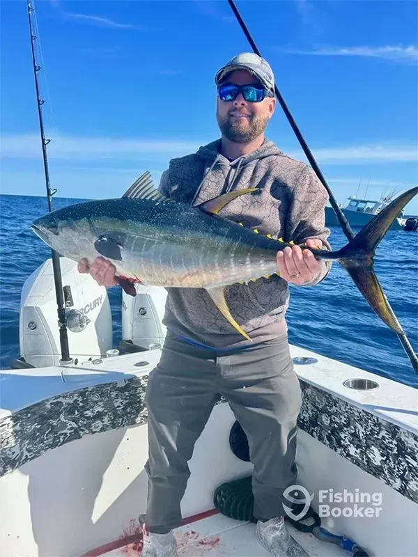 Man on a boat holding a large tuna under a bright blue sky