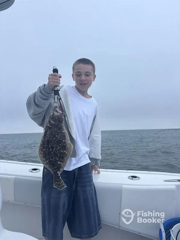 Person on a boat holding up a large fish by the tail against a cloudy ocean backdrop