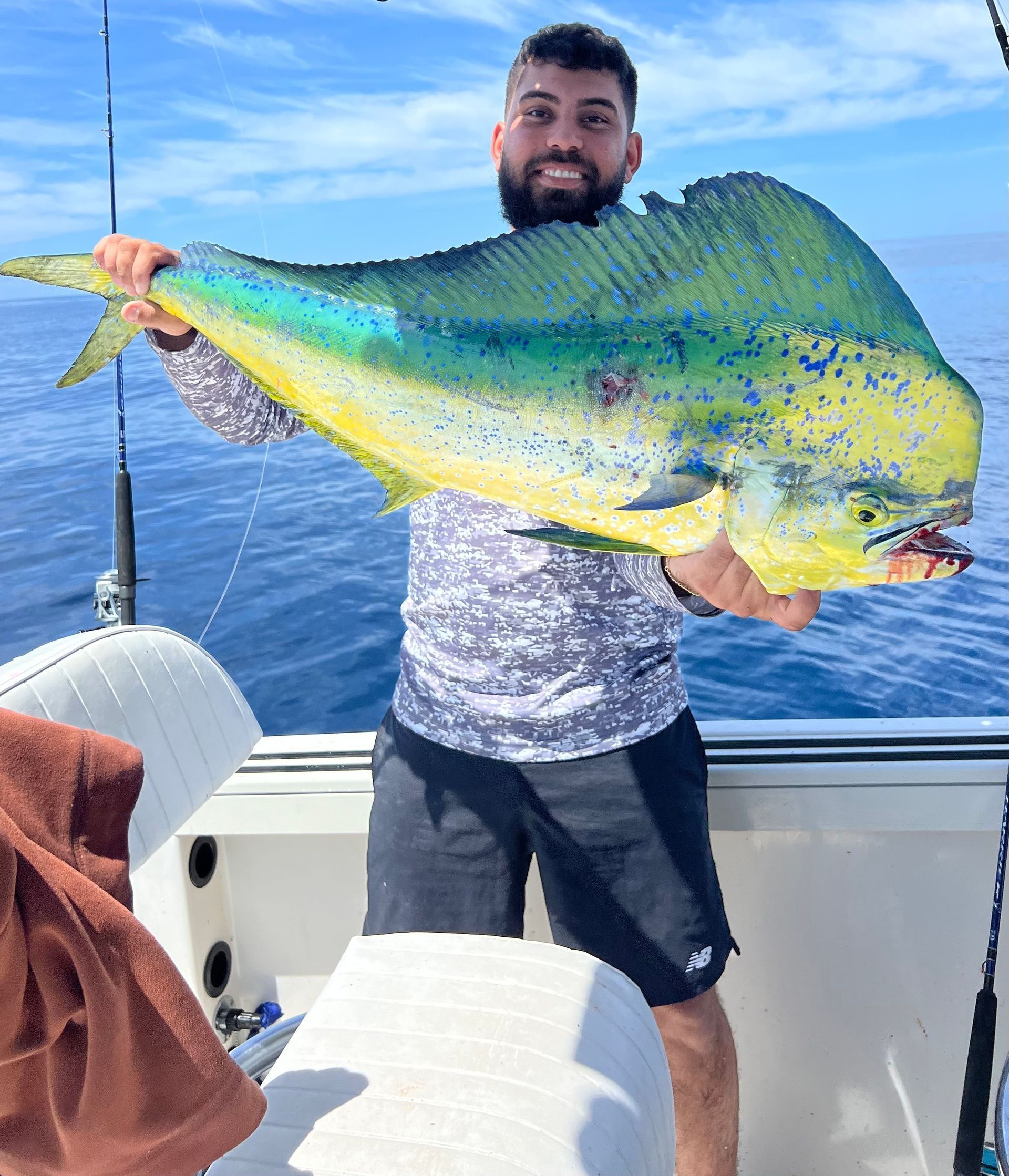 Man holding a large blue-and-yellow fish on a boat with open water behind him
