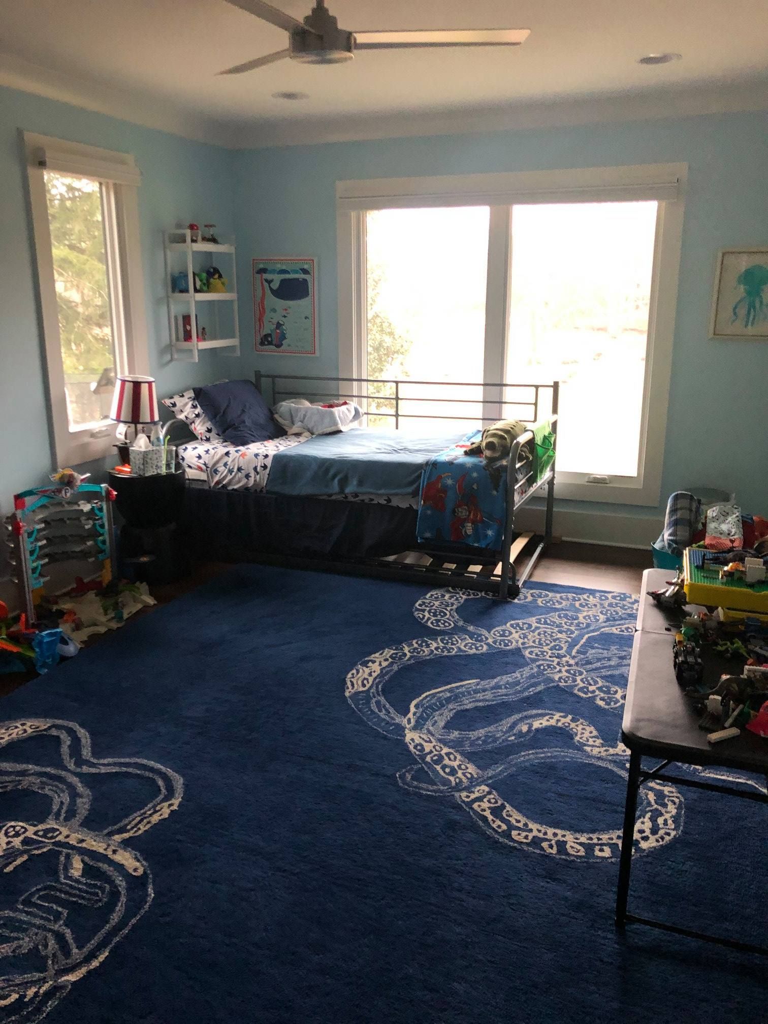 Blue-themed child's bedroom with a bed, toys, and a rug with a track design.