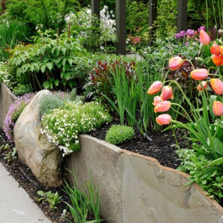 Colorful flowers and greenery in a landscaped garden bed beside a stone retaining wall