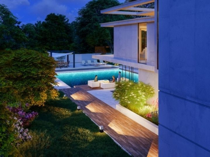 Luxury home terrace with glowing pool, wooden deck, and lush garden at dusk