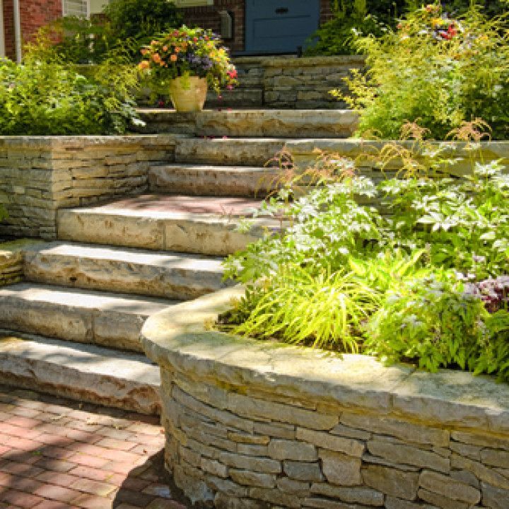 Stone garden steps with brick paths and lush green landscaping leading to a house entrance