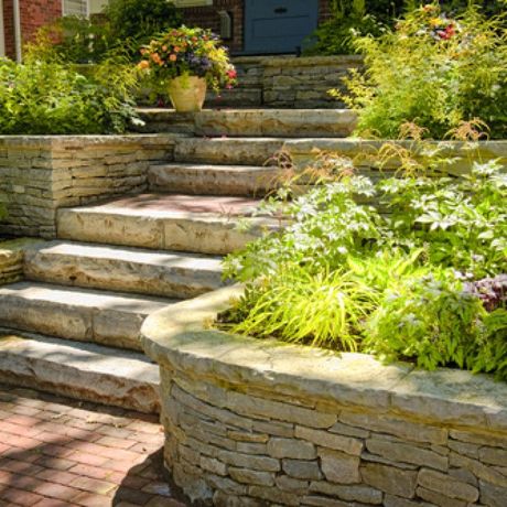Stone steps and curved retaining walls in a lush garden with potted flowers and greenery