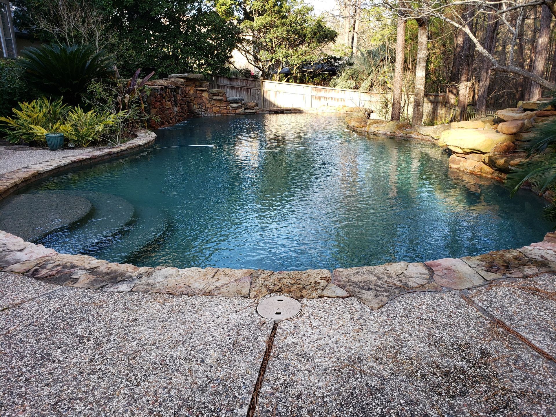 A large swimming pool surrounded by rocks and trees in a backyard.