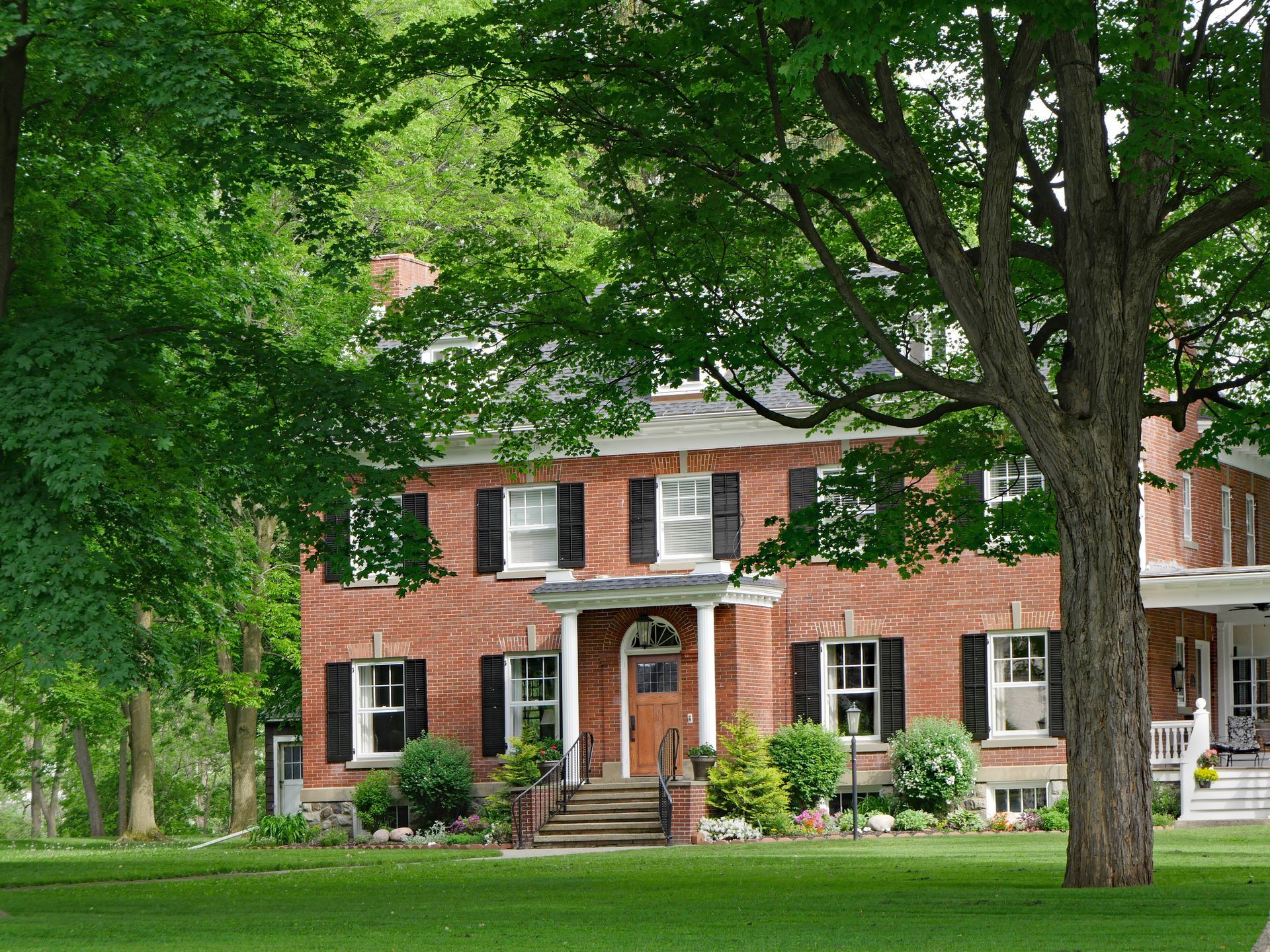 Red brick house with black shutters, green lawn, and large tree.