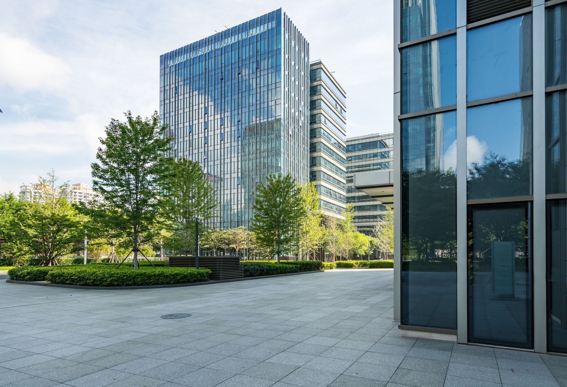 Modern glass office buildings with trees and a paved plaza.