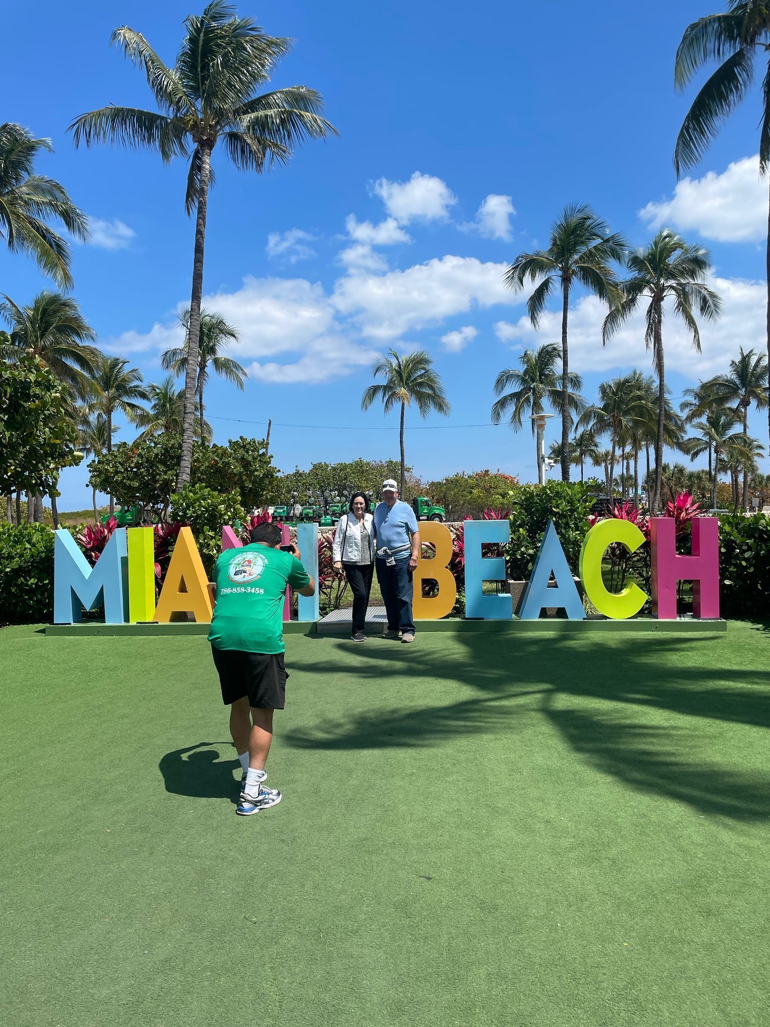 Miami city tour guide taking guest photo in front of colorful Miami Beach sign on a sunny day
