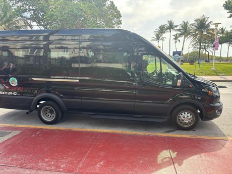 Black Miami sightseeing van parked along Ocean Drive with palm trees in the background”
