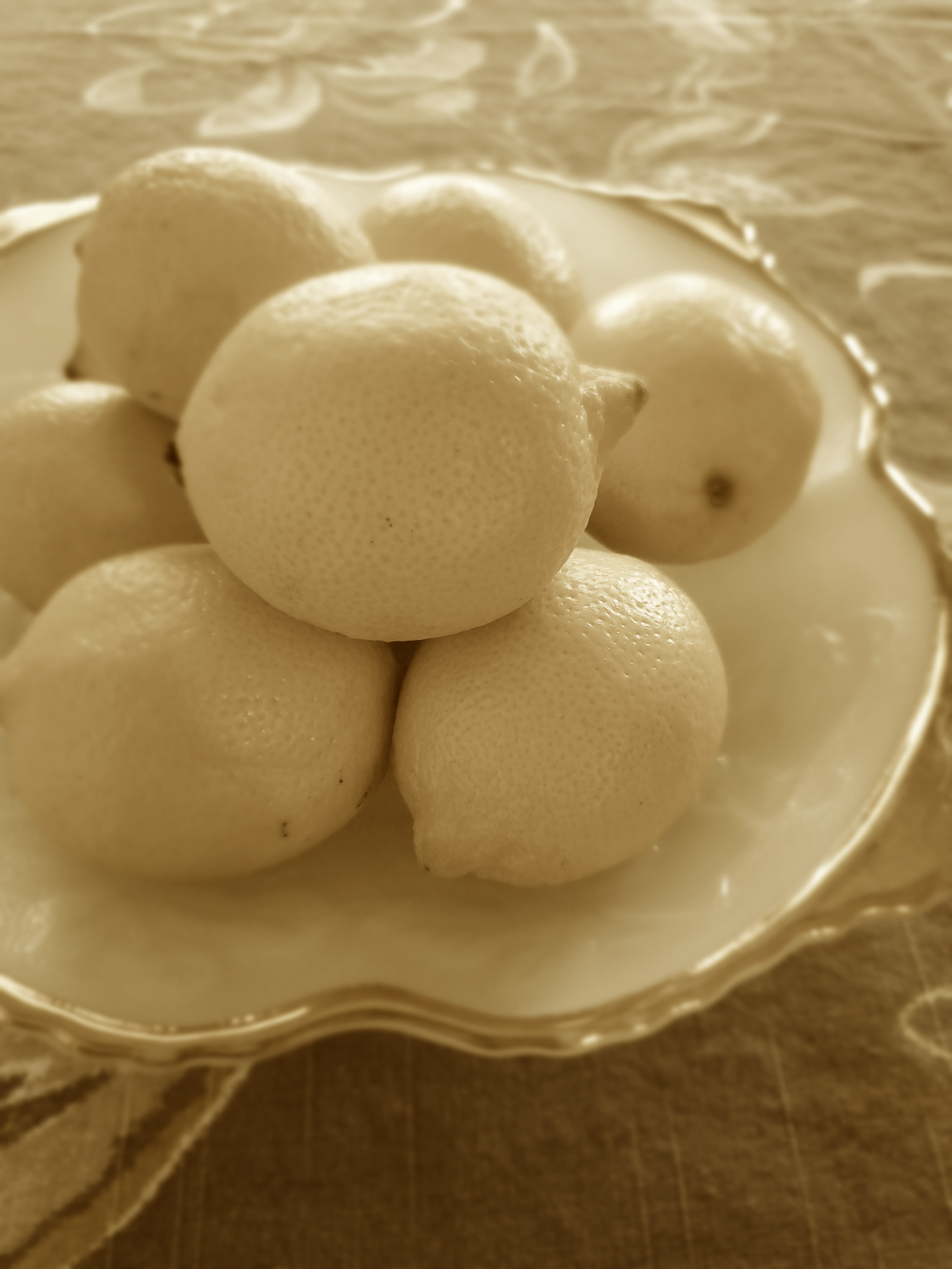 Lemons in a white and gold-rimmed bowl on a brown patterned surface.
