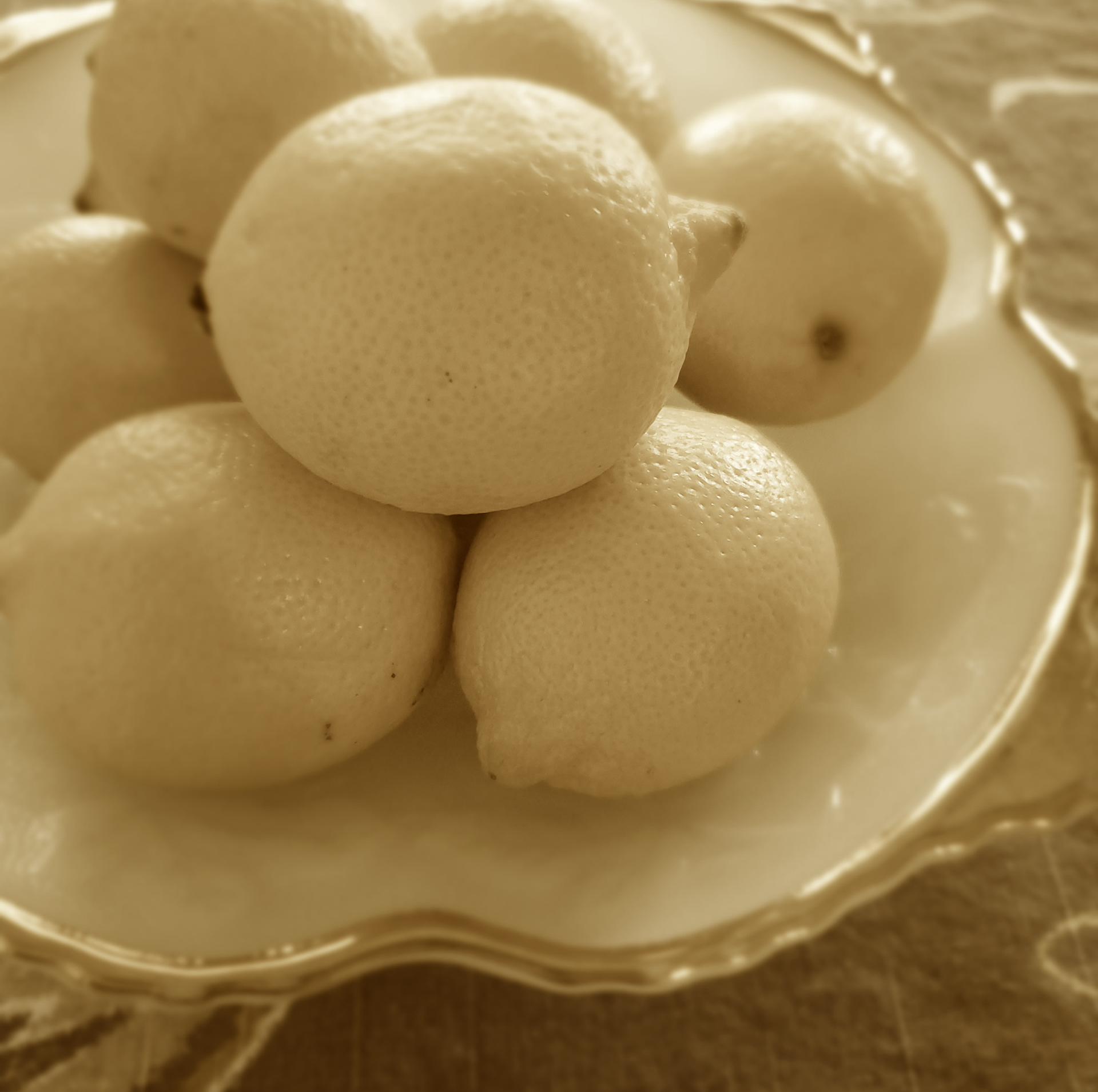 Lemons piled on a decorative plate, sepia-toned.