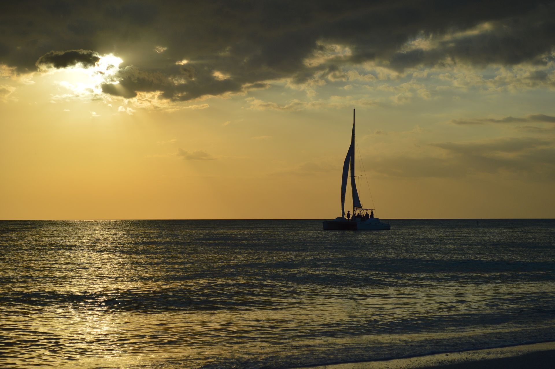 Sailboat on ocean at sunset; golden light, dark clouds.