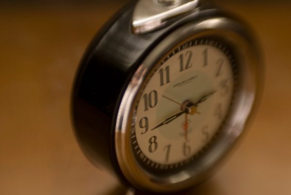 Alarm clock on a wood surface, black and silver, hands showing approximately 9:12.