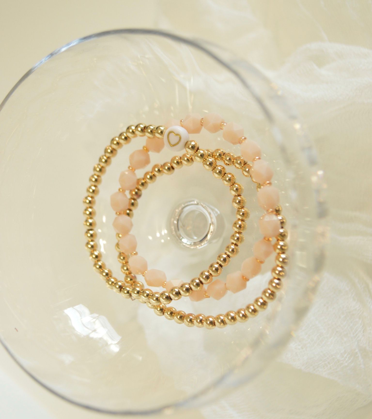 Two gold beaded bracelets with a heart accent inside a glass.
