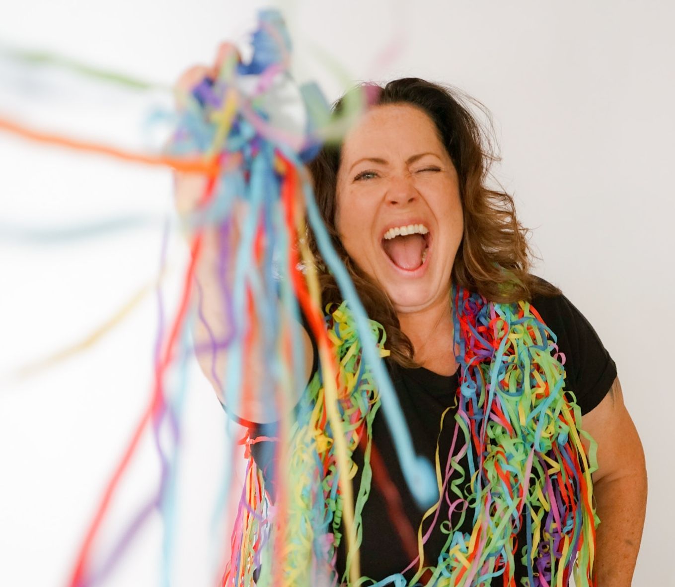 Woman with confetti winking, smiling, and celebrating, indoors with a white background.