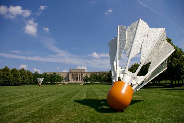 Giant shuttlecocks sculptures on a green lawn in front of a classical building under a blue sky.