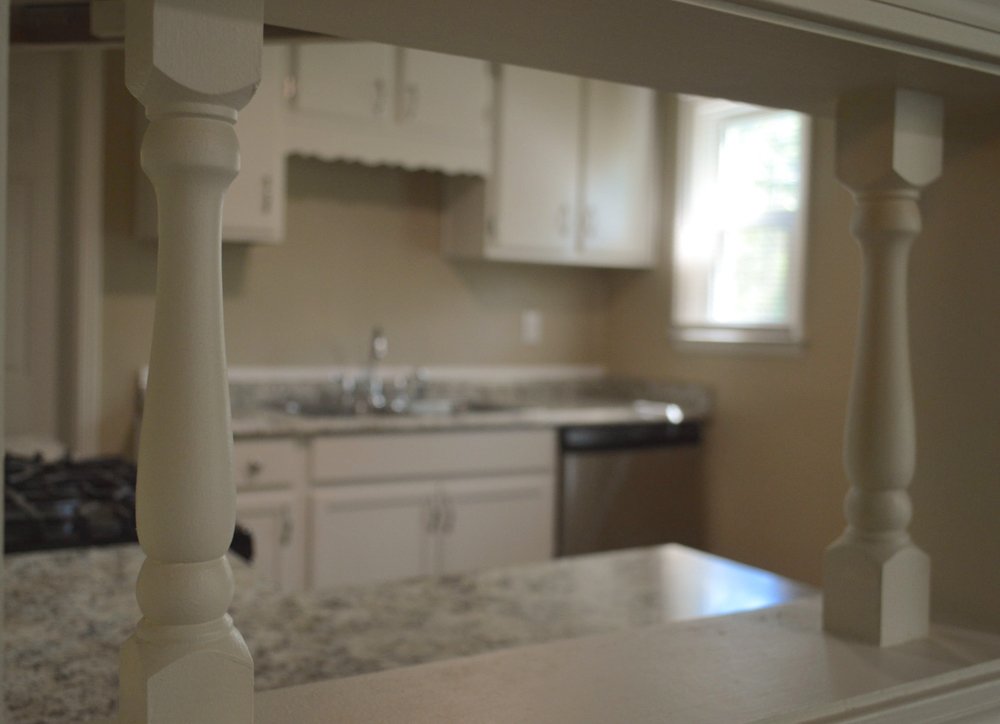 A kitchen with white cabinets and granite counter tops is seen through a window.