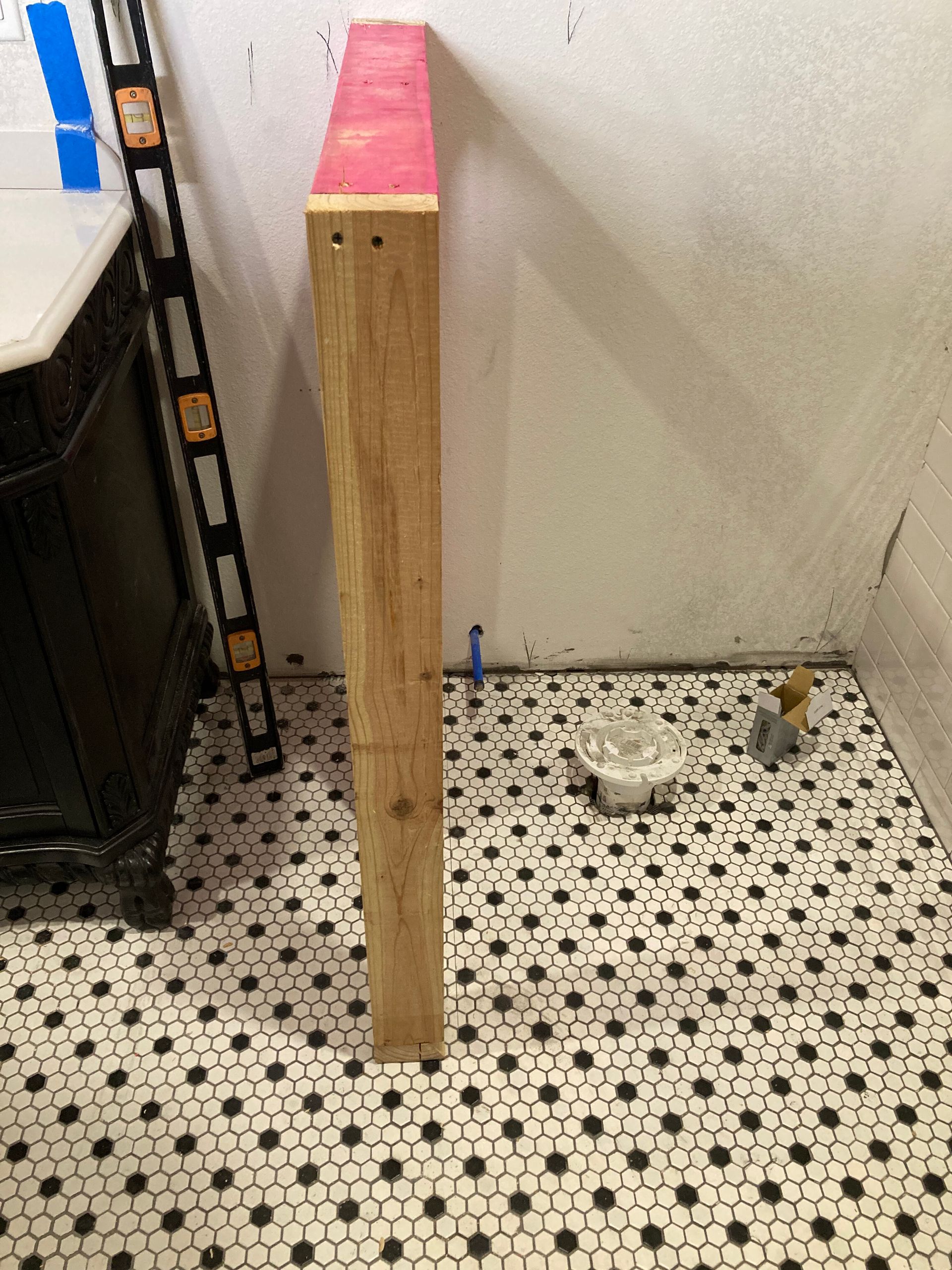Tall wooden board with a red top standing on patterned tile floor against a wall.