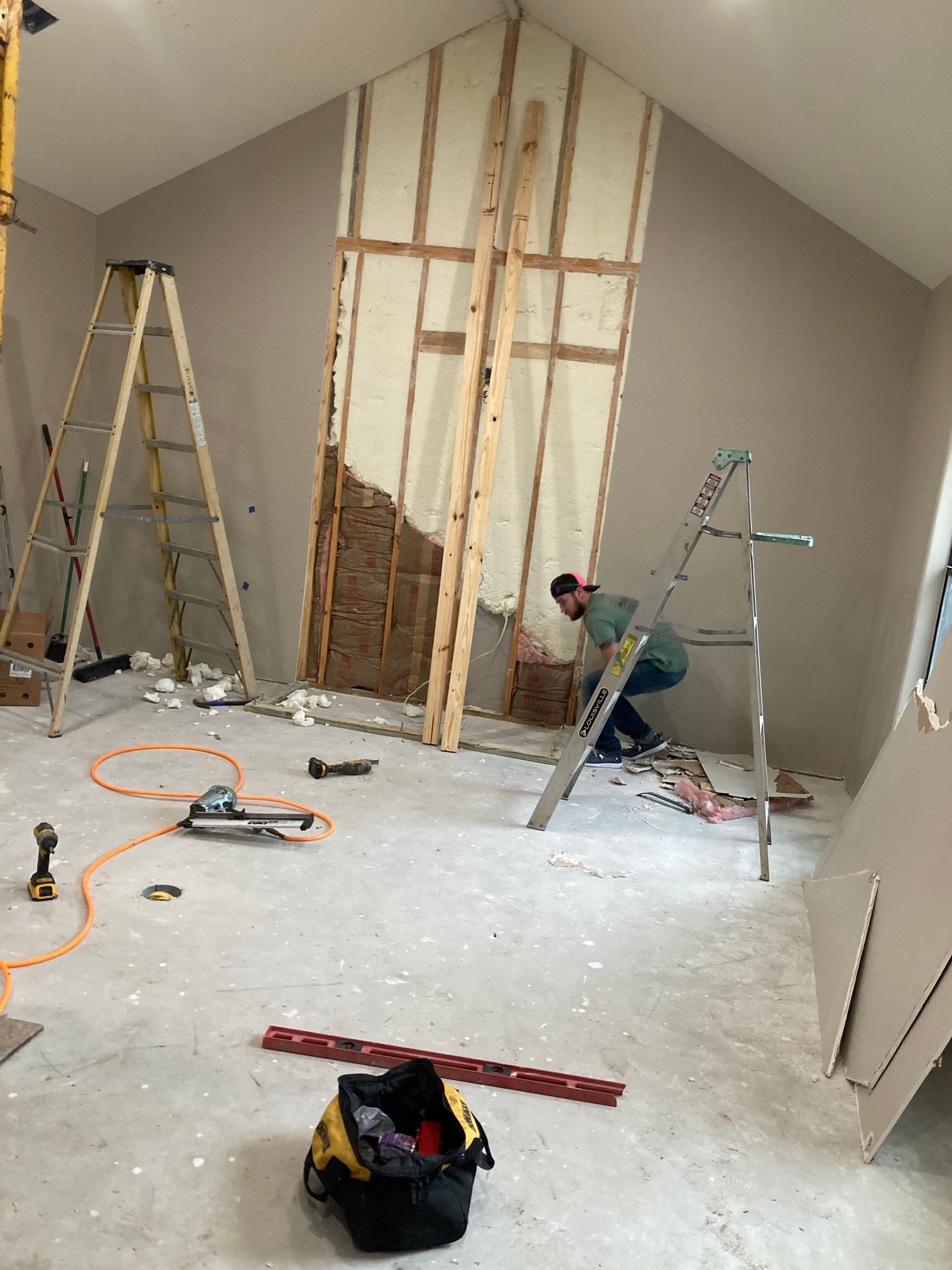 Unfinished attic room under renovation with exposed studs, ladders, tools, and construction debris on the floor
